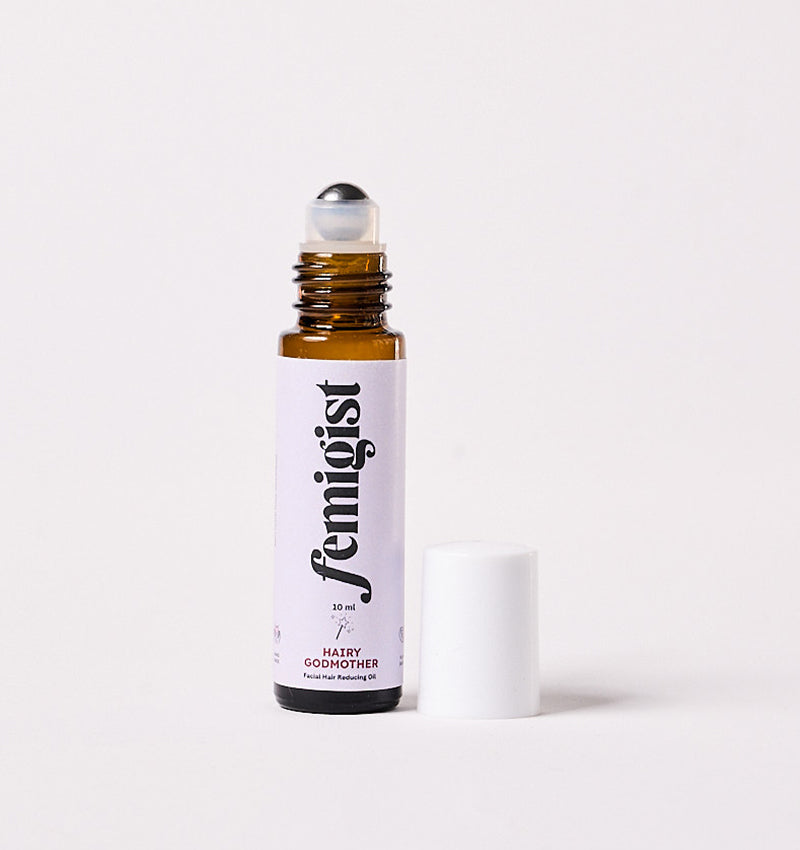 10ml roller bottle of Hairy Godmother facial hair reducing oil by Femigist, with the cap removed and the roll-on top visible, set against a white background.